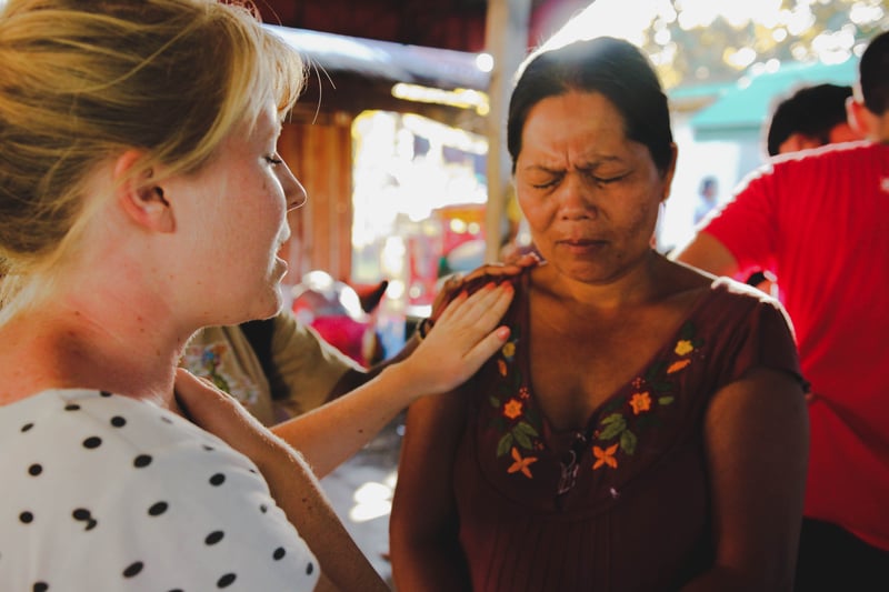 Young YWAM missionary woman praying for a lady while on outreach in the Philippines