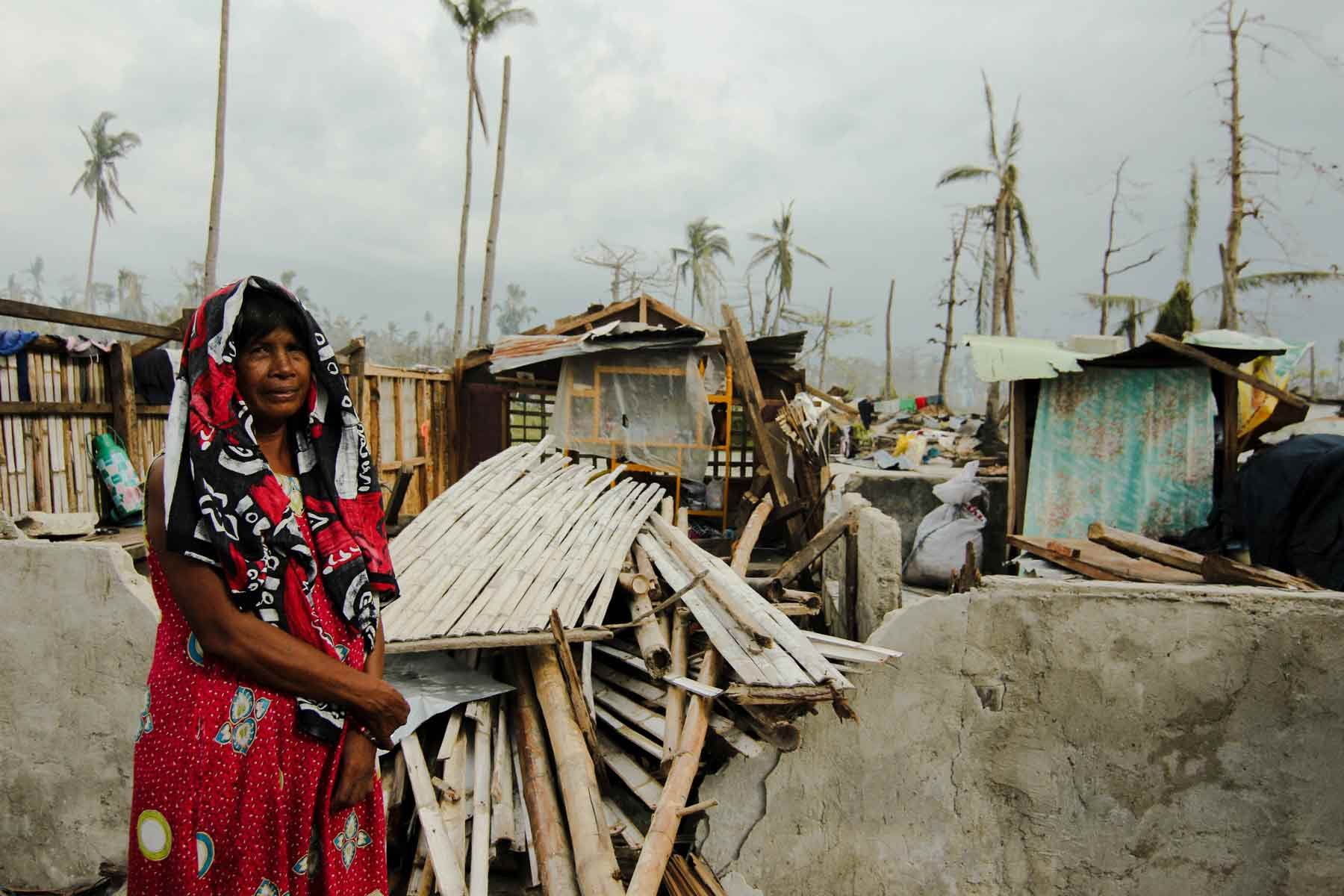 Woman standing in front of destroyed shack in tropical country