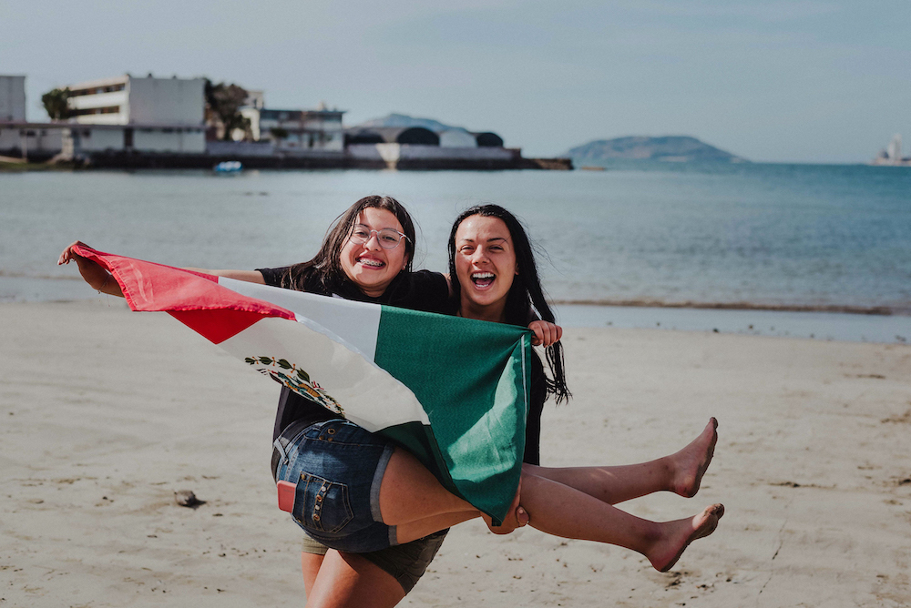 YWAM missionary girls holding a Mexican flag on the beach near YWAM Mazatlan, Mexico